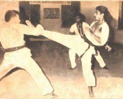 In 1981, during a Shodan-level kumite match, I am facing a front kick from Sensei Johnny Jose, an accomplished Karate fighter. Sensei P. Kuppusamy can be seen officiating the bout as referee. front kick